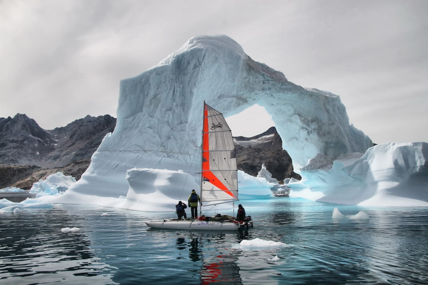 Ducky19, un catamarán hinchable con una vela roja y blanca, navegando cerca de un iceberg